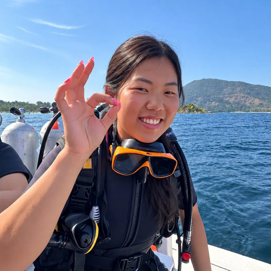 Liang in duikuitrusting op een boot in Thailand, met een OK-teken naar de camera